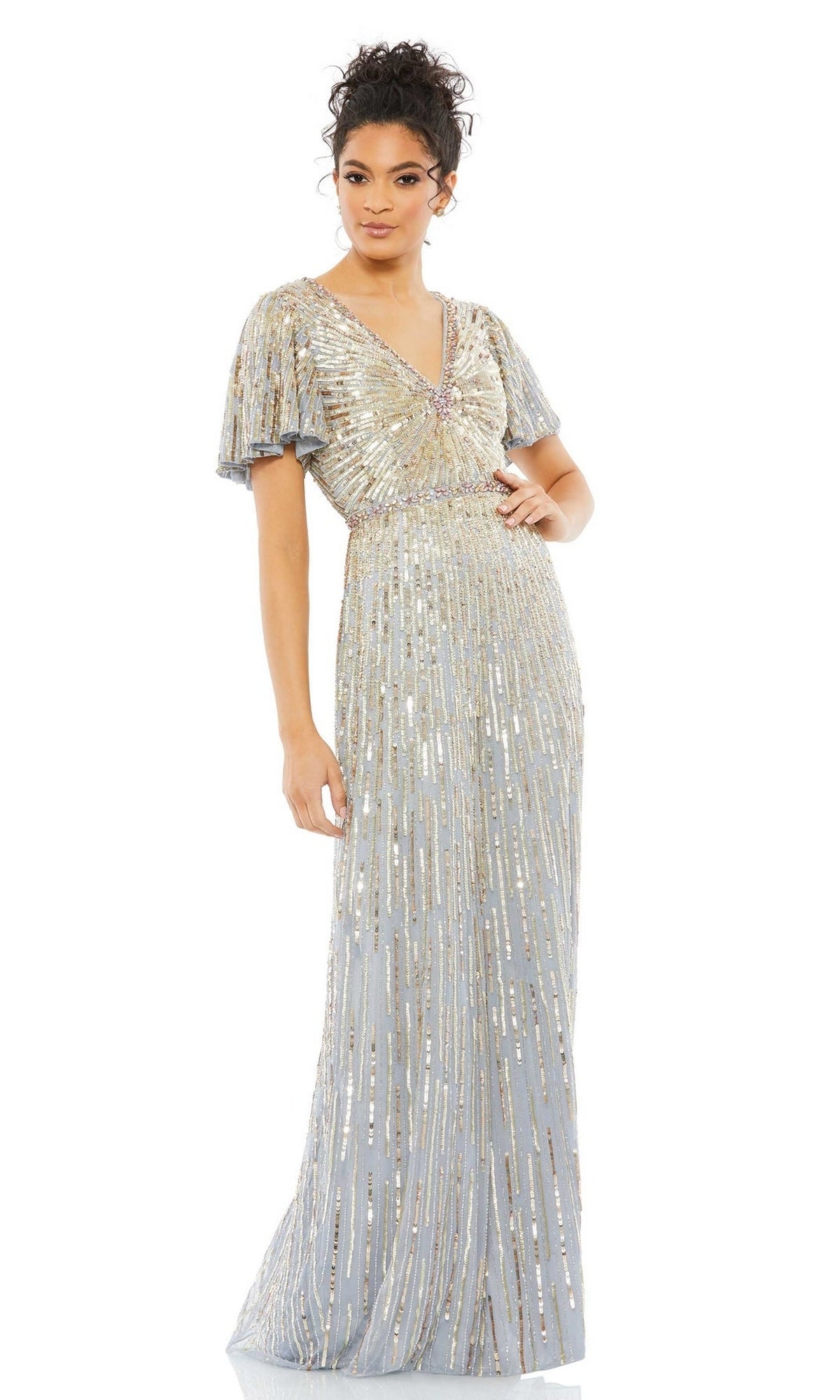 A woman stands wearing the Long Formal Dress 5538 by Mac Duggal, a floor-length light blue sequin gown with a V-neckline, gold and silver embellishments, and elegant short butterfly sleeves.